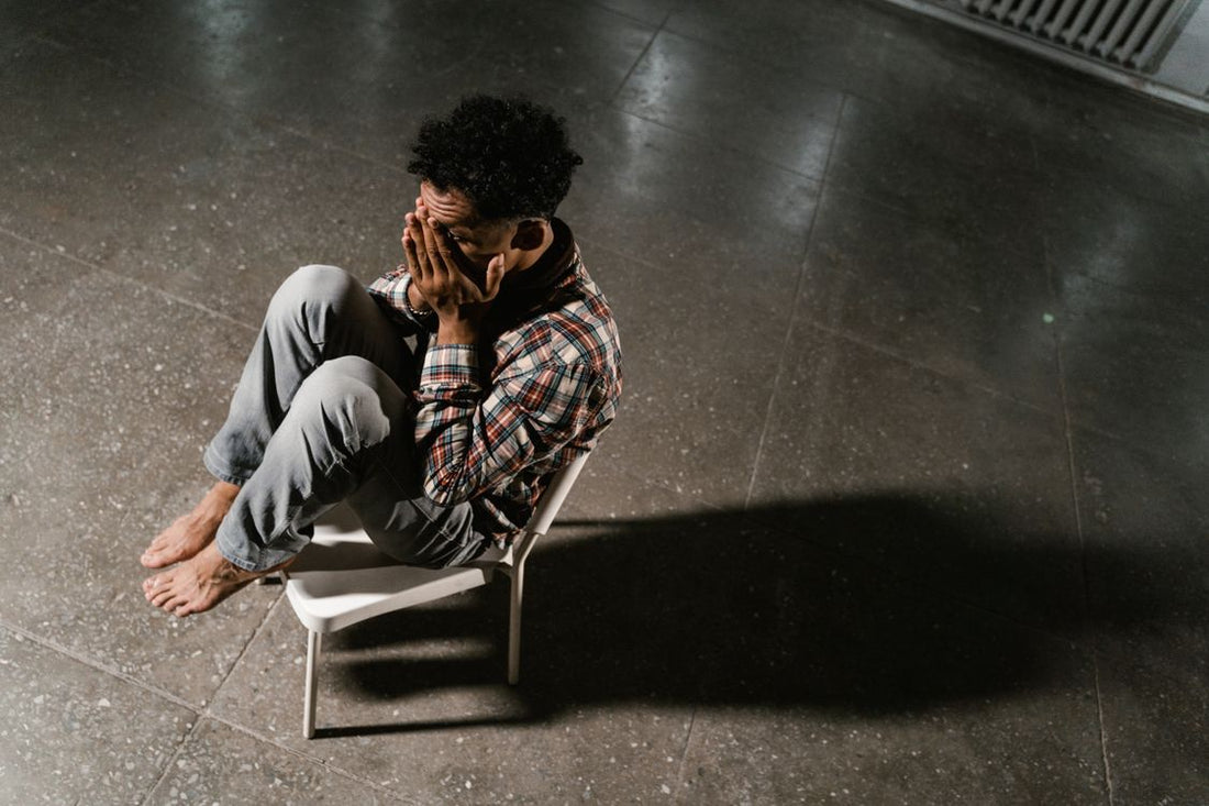 A man sitting alone in a dim room, head down, showing signs of low confidence and stress